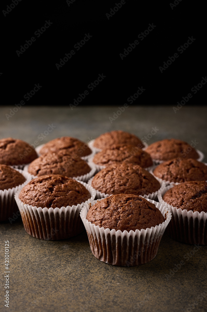 Homemade chocolate cupcakes in baking paper forms on wooden background, selective focus, close up, vertical orientation
