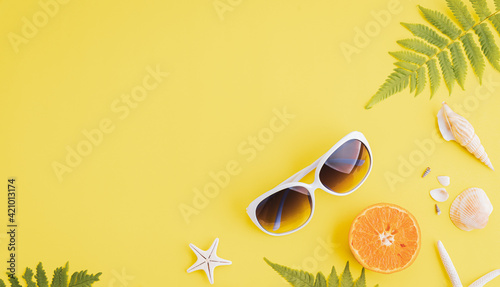 Summer holiday and vacation concept, including beach accessories sunglasses, starfish, orange, fern leaves and sea shell on yellow background.