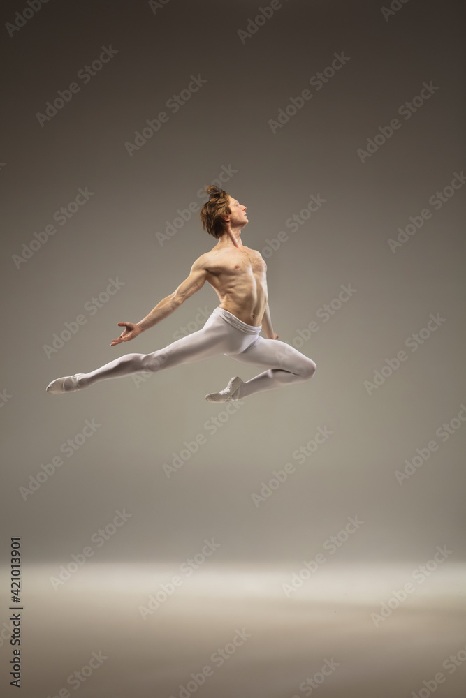 Flying bird. Young and graceful ballet dancer isolated on studio background in flight, jump. Art, motion, action, flexibility, inspiration concept. Flexible caucasian ballet dancer, moves in glow.
