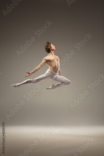 Flying bird. Young and graceful ballet dancer isolated on studio background in flight, jump. Art, motion, action, flexibility, inspiration concept. Flexible caucasian ballet dancer, moves in glow. © master1305