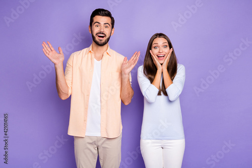 Photo of amazed man and woman couple raise hands hold cheekbones lucky discount isolated on violet color background