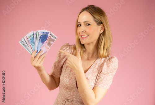 Excited woman holding money banknotes over pink background