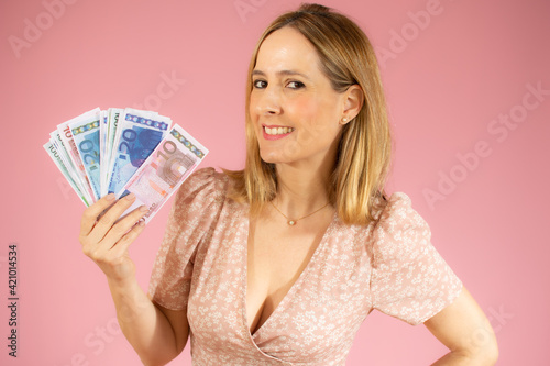 Excited woman holding money banknotes over pink background