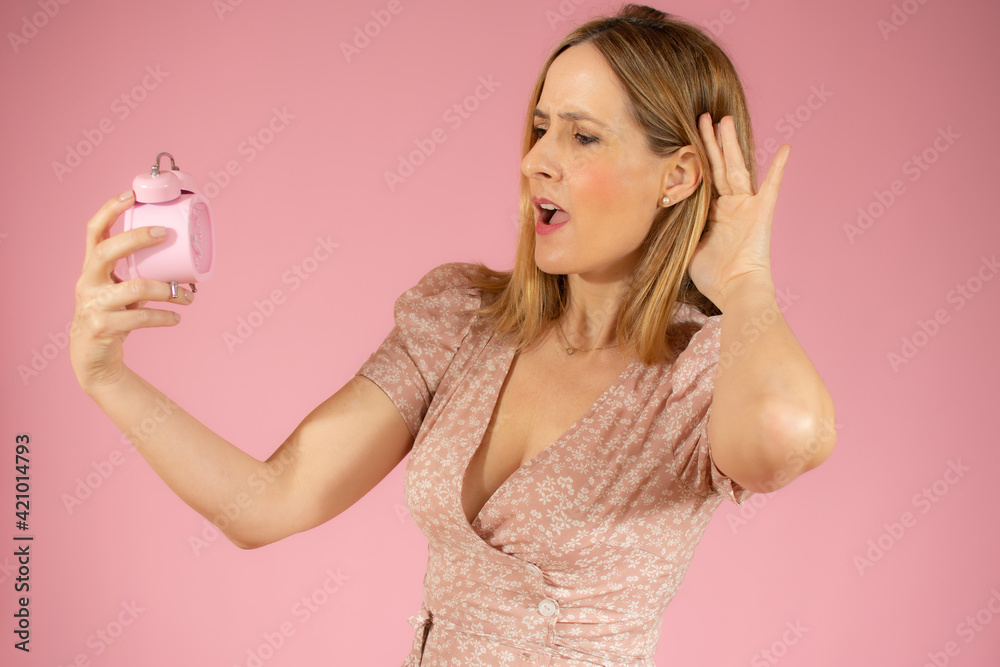 Young surprised woman holding classic alarm clock over isolated pink background Young surprised woman holding classic alarm clock over isolated pink background
