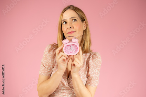 Young caucasian woman holding classic alarm clock over isolated pink background