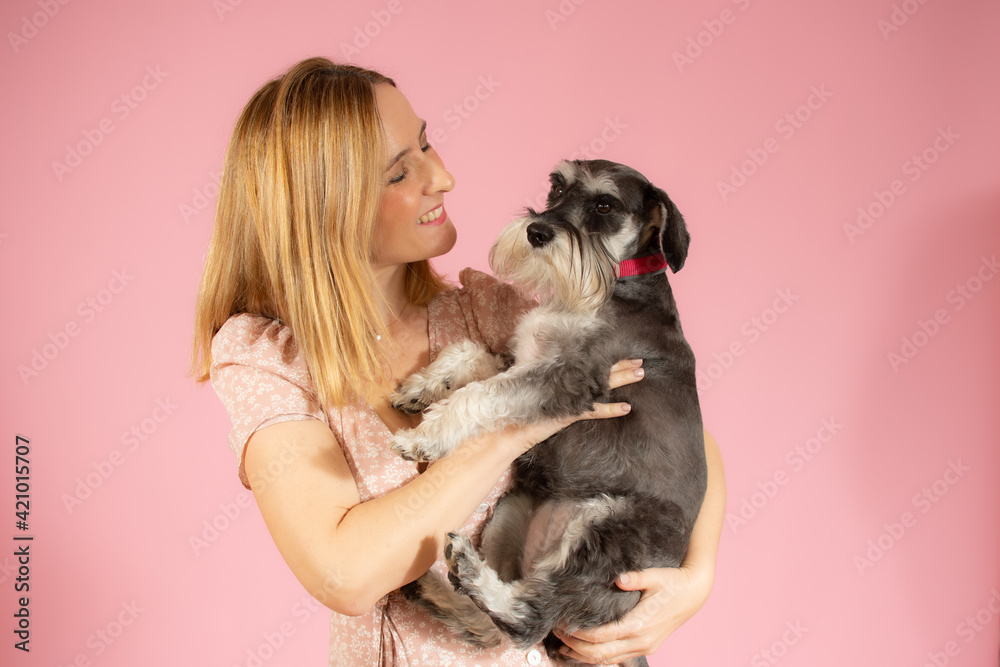 Cute young woman hugs her puppy schnauzer dog. Love between owner and dog isolated over pink background. Studio portrait. Cute young woman hugs her puppy schnauzer dog. Love between owner and dog isolated over pink background. Studio portrait.