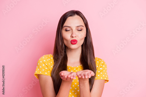 Photo of flirty attractive young woman send air kiss hands you closed eyes isolated on pastel pink color background