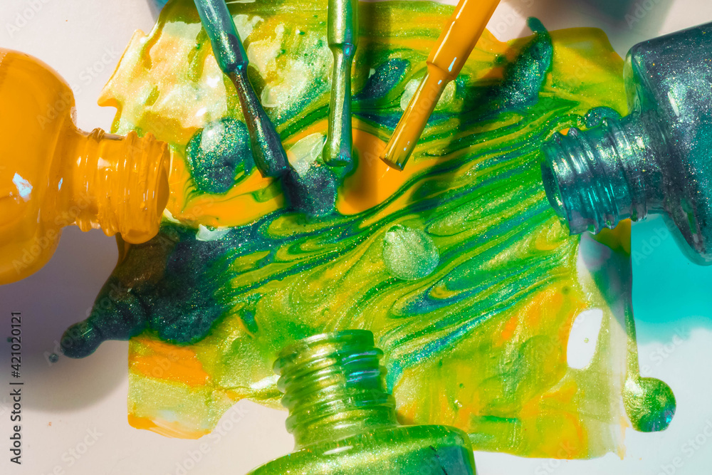 Bright nail polish in green, yellow, blue colors with sparkles spilled