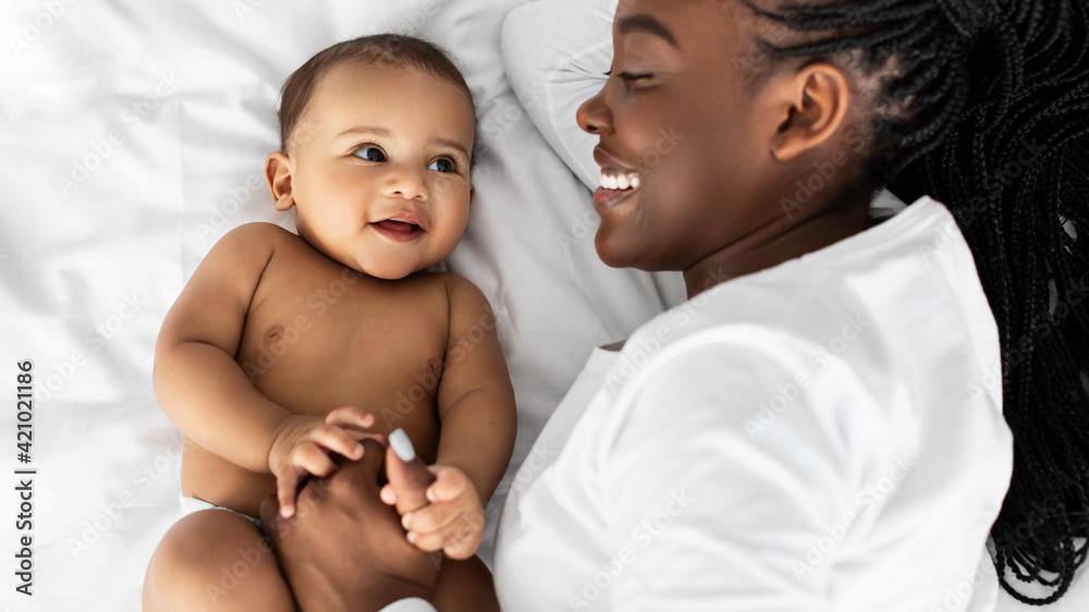 African American mom lying in bed with her cute baby