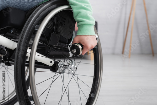 Cropped view of woman holding dumbbell near wheel of wheelchair