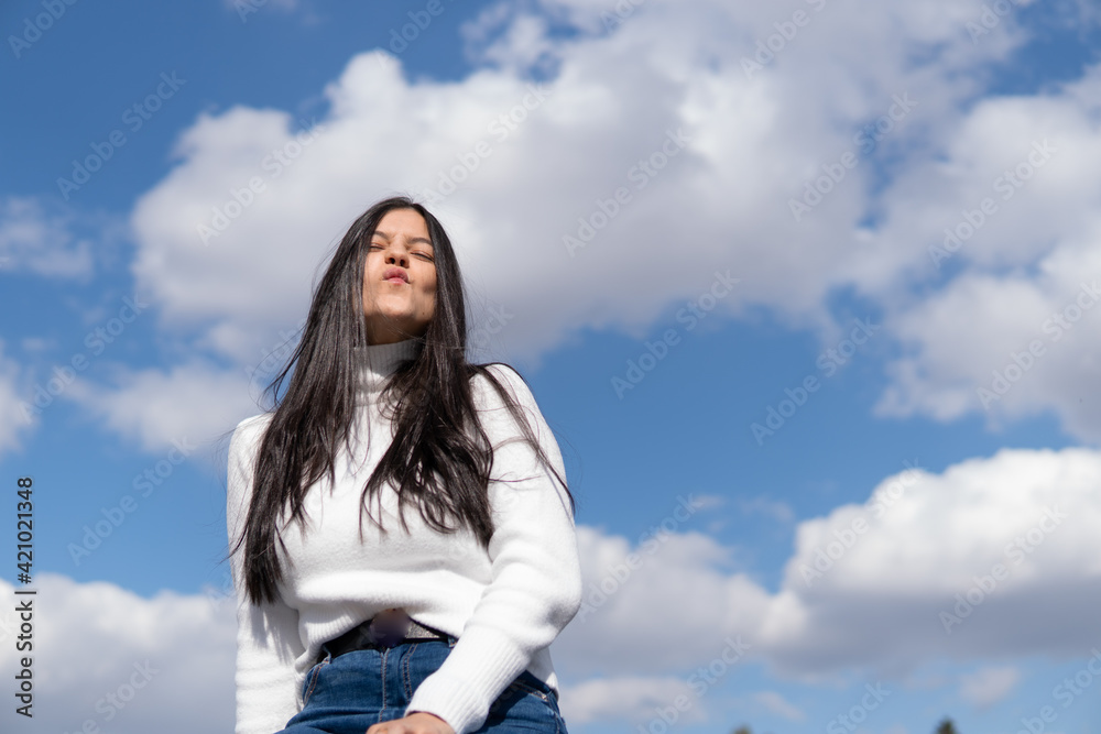 Young girl in blue jeans and white sweater with blue sky in the background Young girl in blue jeans and white sweater with blue sky in the background