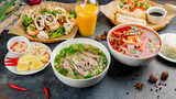 Assorted asian dinner, vietnamese food. Pho bo, pho tom, noodles, spring rolls, tom yam, rice, mango shake on beautiful black stone table