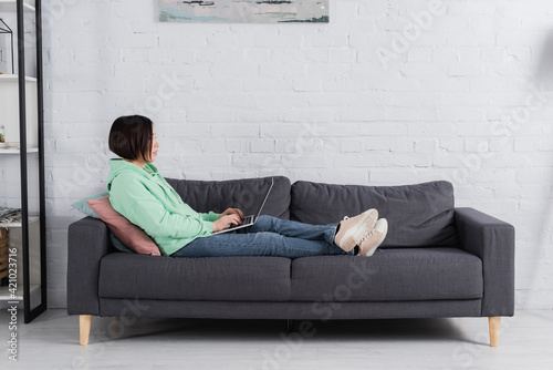 Side view of freelancer using laptop on couch in living room