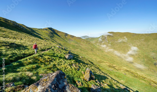 Obraz na płótnie A female hiker and their dog walking towards the mountain summit of Meall Corranaich with the mountain ridge of Ben Lawers and Beinn Ghlas above in the Scottish Highlands, UK landscape. w salonie