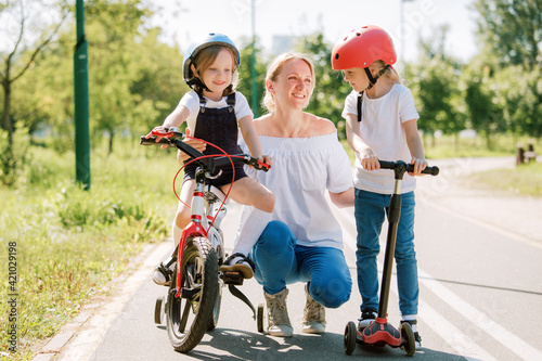 Mother with two chherful daughters having fun. Woman and girls in helmets riding on bicycle and scooter