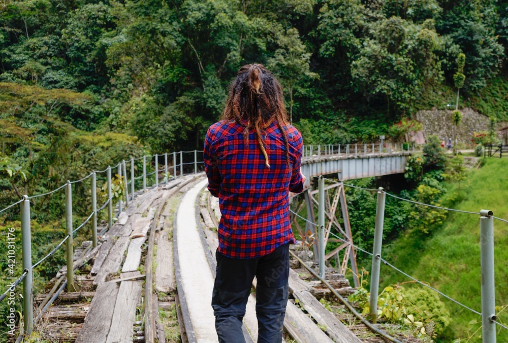Naklejka premium Man from behind with dreadlocks and square shirt standing on the train tracks on a bridge