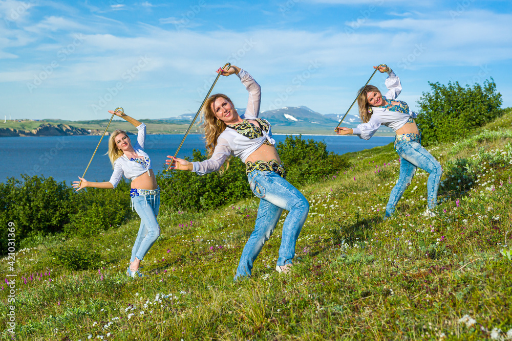 A group of european women dancing oriental dances with a cane on the background of the sea and snow-capped mountains in the tundra in summer