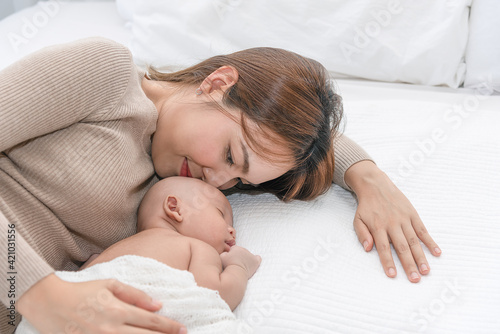 Close up beautiful young asian mother kissing her newborn one month baby sleep in bed. Healthcare and medical love asia woman lifestyle mother's day concept.