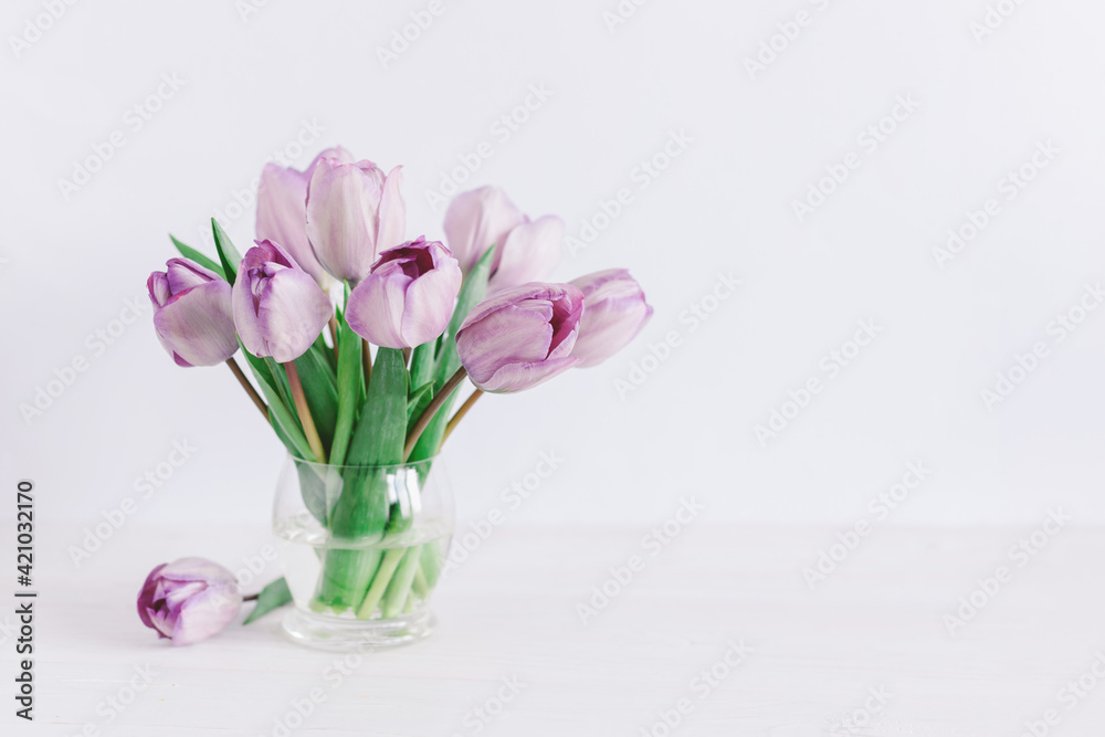 Tender violet tulips in a vase on a white wooden background. Greeting card for Women's day. Tender violet tulips in a vase on a white wooden background. Greeting card for Women's day.