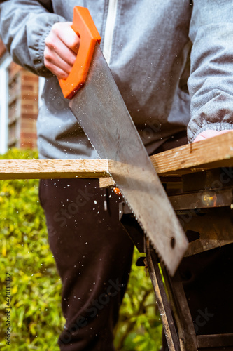 Young male sawing wood on a work bench.