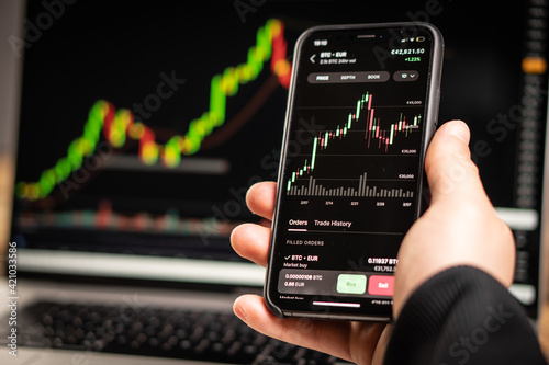 A man holds a phone in his hand and trades in cryptocurrencies on the stock exchange.