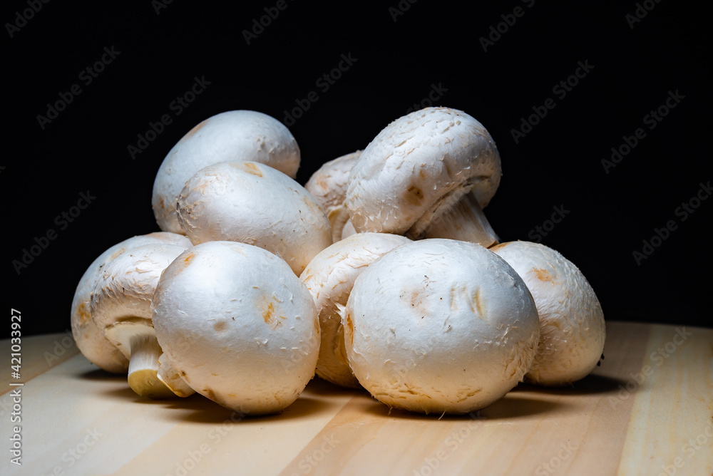 closeup big white delicious champignon mushrooms lie on a wooden board, ready to cook on a black background