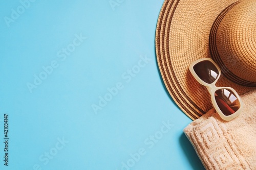 Summer travel beach essentials top view photography. Yellow straw hat, brown sunglasses and beige towel on a blue background. Mockup, flat lay image, free space for text
