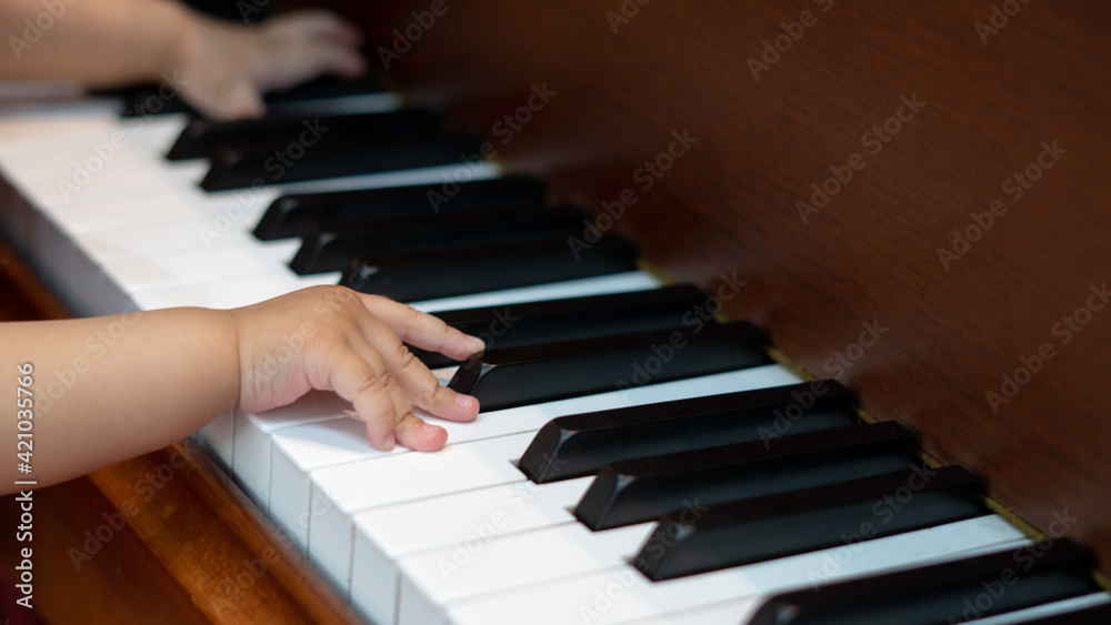 Fototapeta premium Side view of Baby Girl's Hands playing with Piano Keys with an adult