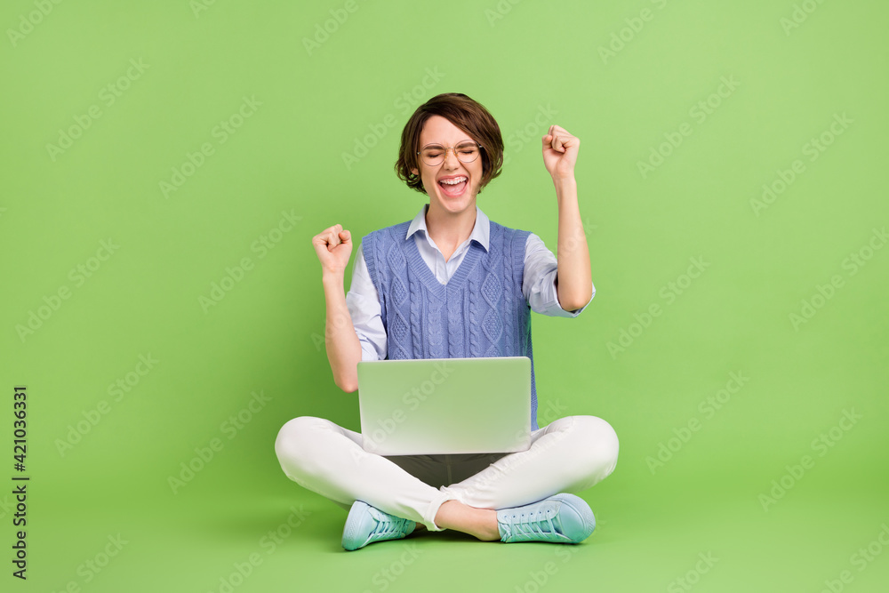 Portrait of attractive dreamy lucky cheerful girl sitting lotus position using laptop rejoicing isolated over green color background Portrait of attractive dreamy lucky cheerful girl sitting lotus position using laptop rejoicing isolated over green color background