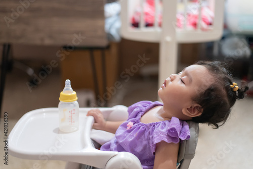 Side view of cute little asian baby girl Sitting asleep on the dining table After eating full in the house photo