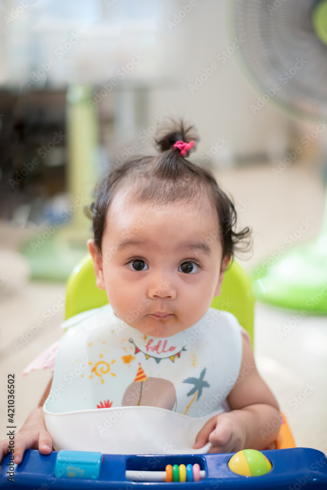 Fototapeta premium Portrait of happy Asian baby sitting on the dining table, looking at the camera