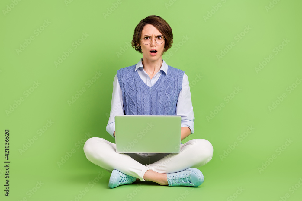 Portrait of attractive mad disappointed girl sitting lotus position using laptop bad news isolated over green color background Portrait of attractive mad disappointed girl sitting lotus position using laptop bad news isolated over green color background