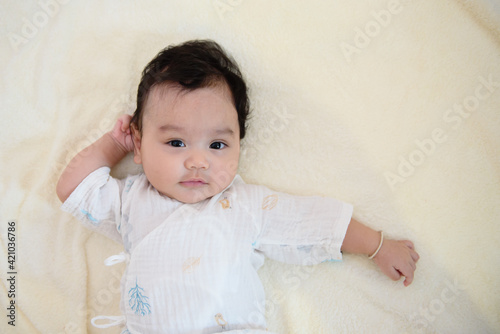 Top view of a cute little Asian baby girl lying on the bed, looking at camera