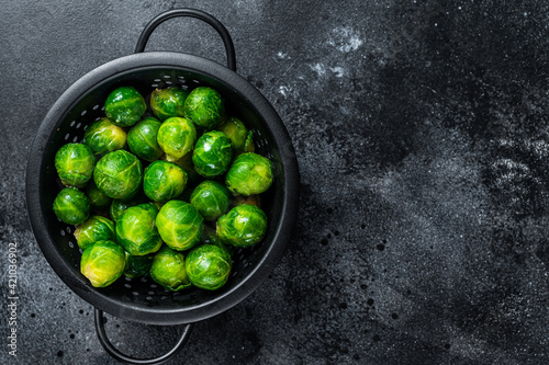Brussels sprouts green cabbage in colander. Black background. Top view. Copy space