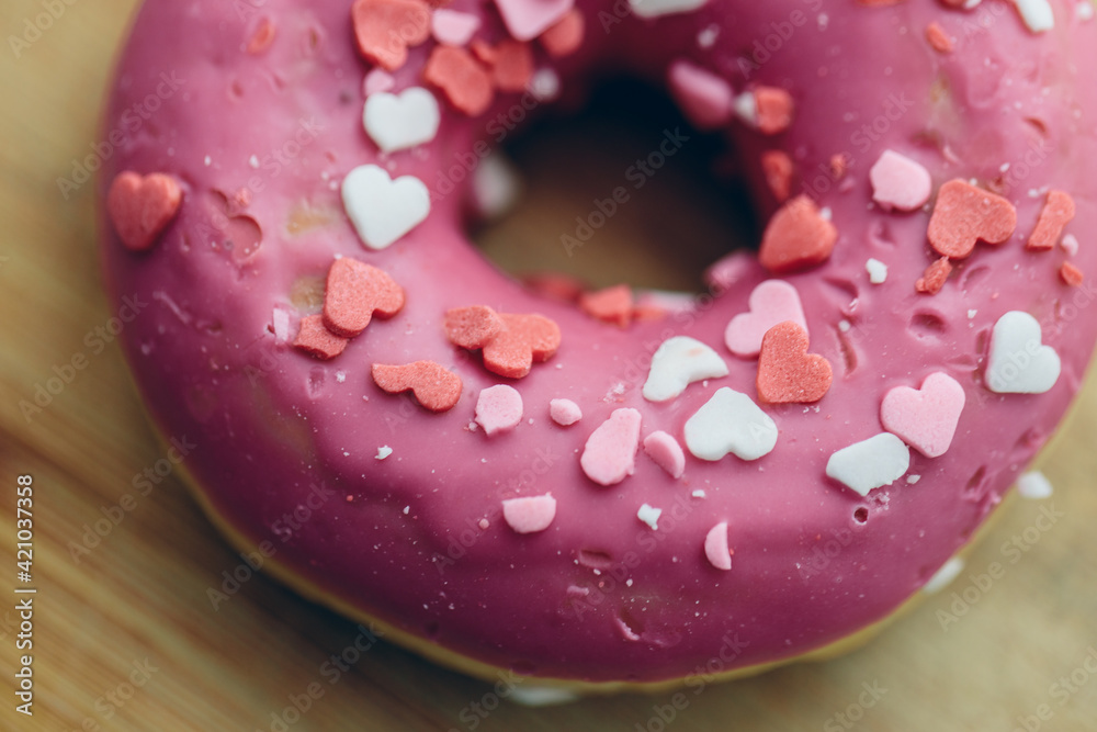 Pink donut decorated with colored glaze in the shape of hearts on an old wooden background. View from above. Close-up.