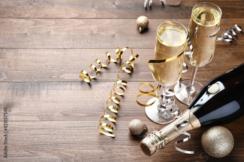 Glasses and bottle of champagne, serpentine streamers with Christmas balls on wooden table. Space for text