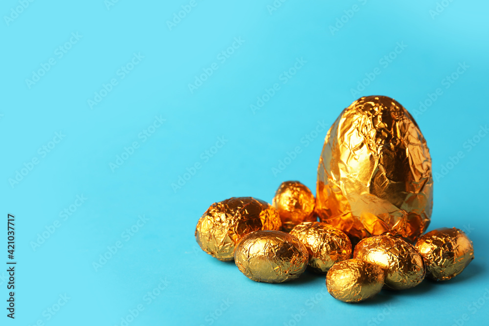 Chocolate eggs wrapped in golden foil on light blue background. Space for text Chocolate eggs wrapped in golden foil on light blue background. Space for text