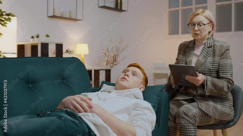 Young man lying on sofa and talking to a psychologist, overcoming bad break-up Young man lying on sofa and talking to a psychologist, overcoming bad break-up