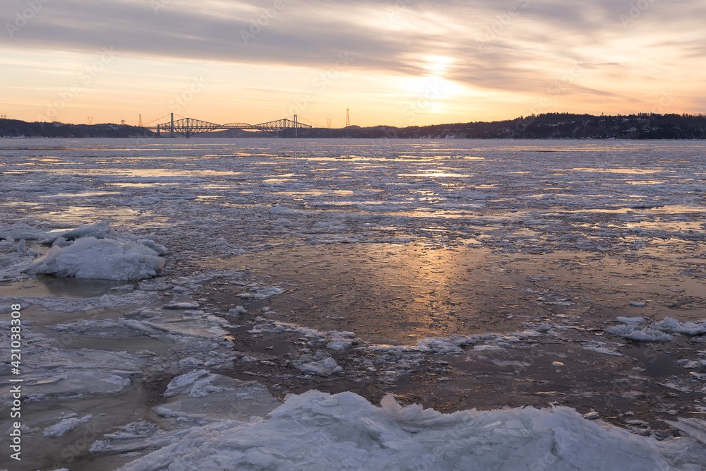 Ice melting on the St. Lawrence River during a hazy late winter sunrise, with the Pierre-Laporte and Quebec bridges in soft focus background, Cap-Rouge area, Quebec City, Quebec, Canada