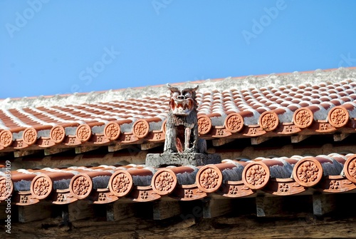 Okinawa shisa sits on a traditional Okinawan red ceramic tile roof. Shisa  is a traditional Ryukyuan cultural artifact and decoration derived from Chinese guardian lions to ward off evil spirits. photo