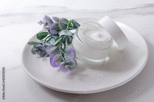 Closeup of glass jar of moistuzing cream, eucaluptys leaves on the plate, white table photo