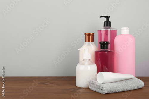 Different shower gel bottles with towel on wooden table. Space for text