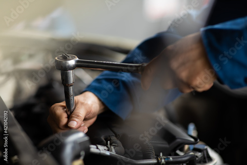 Caucasian male mechanic repairs car in garage. Car maintenance and auto service garage concept. Close up mechanical hand and spanner.