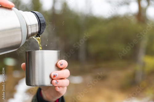 Youg beautifull women pouring beverage from termos to cup in a cold raini day. Healthy living and hiking. photo