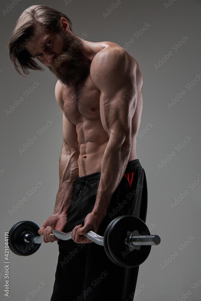 Topless sportsman holding heavy barbell looks down in gray background Topless sportsman holding heavy barbell looks down in gray background