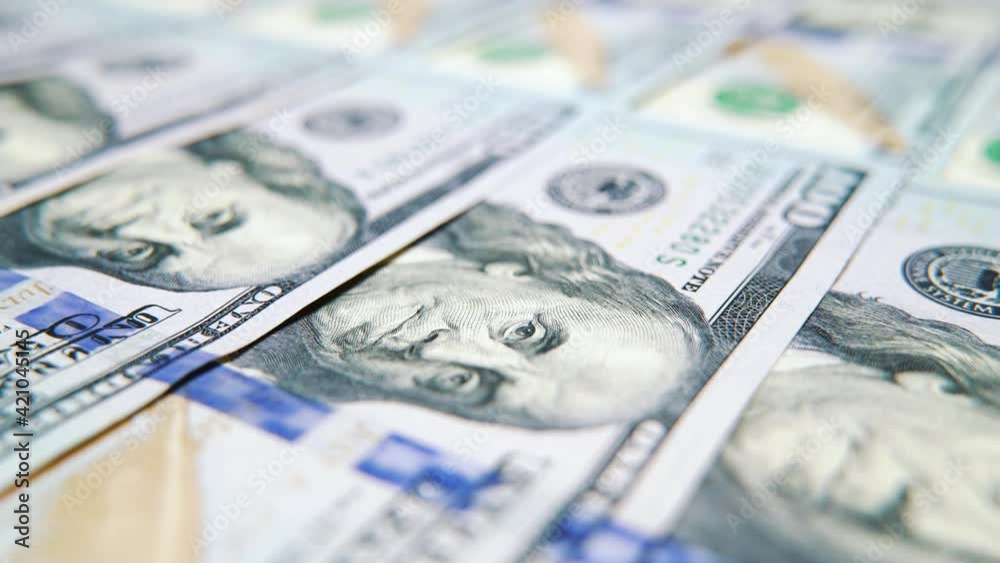Macro of American dollars arranged accurately on surface, focus on face of Benjamin Franklin. Tracking shot of banknotes symbolizing wealth and prosperity. Concept of money