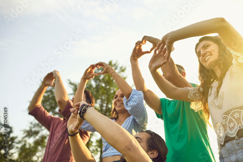 Happy young friends making hearts with hands in countryside at sunset. Group of volunteers expressing love outside