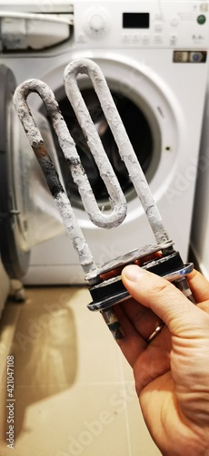 Washing machine repair. A man holds in his hand an old, faulty heating element of a wash.  photo