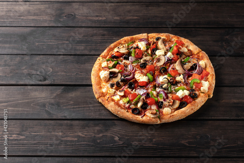 whole fresh round pizza with chicken meat, vegetables, mushrooms and cheese close-up on a wooden brown table