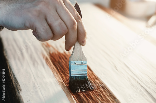A working cabinetmaker holds a brush in his hand and paints a wooden surface. A trace of paint on a wooden board. photo